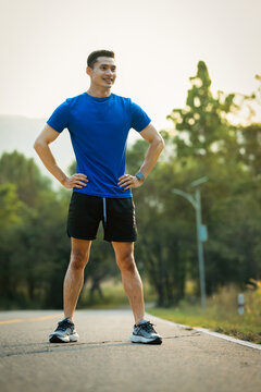 Full length of male athlete in fitness clothes posing outdoor, keeping hands on waist and looking away
