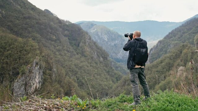 An adult Caucasian professional photographer taking pictures with a digital camera while hiking in the mountains. 