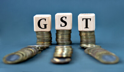 GST - acronym on wooden cubes against the background of stacks of coins