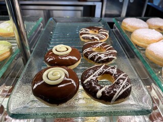 Assorted glazed donuts with chocolate sprinkles topping inside a shop counter