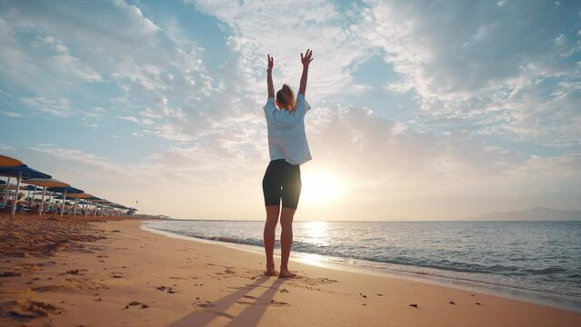 Barefooted woman doing yoga standing on one leg balancing in tree pose on sandy sea ocean beach at sunset. Female stretching relaxing concentrating on asana. Body care wellness sport activity concept.