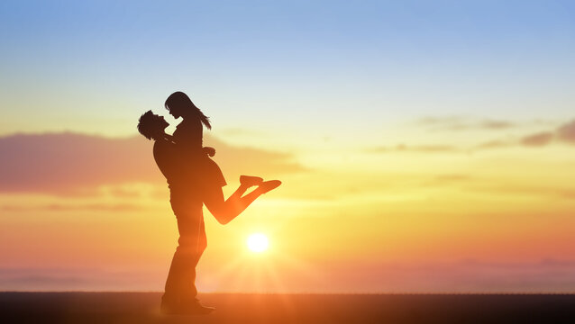 Couple kissing with beautiful sunset in background, man lifting woman. Couple in love silhouette during sunset, backlit. copy space