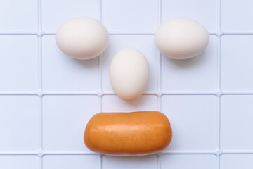 Comic face of three eggs and sausages on a plastic checkered surface