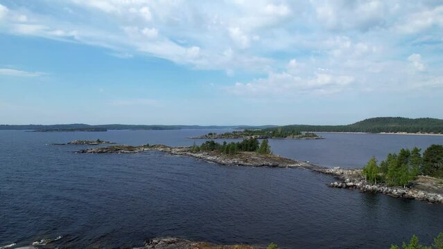 Aerial Drone Footage View: Flight over a rocky island covered with green forest. Panoramic view of the coastline with numerous bays and skerries. Clear blue water of a large lake. Lake Ladoga, 4K