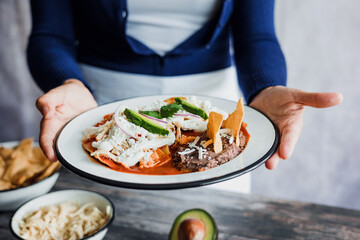 Mexican woman hands preparing chilaquiles with red sauce and eating traditional mexican food for breakfast in Mexico Latin America, hispanic people