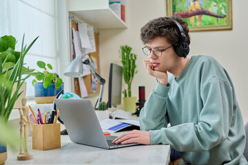 Young male college student sitting at desk at home using laptop