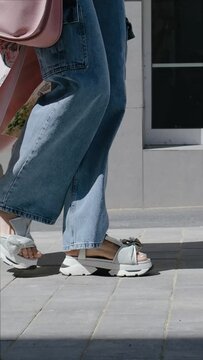 Close up Female legs walking. Woman in trendy cargo jeans and open sandals on high platform wedge. Summer or spring stylish clothes and shoes.