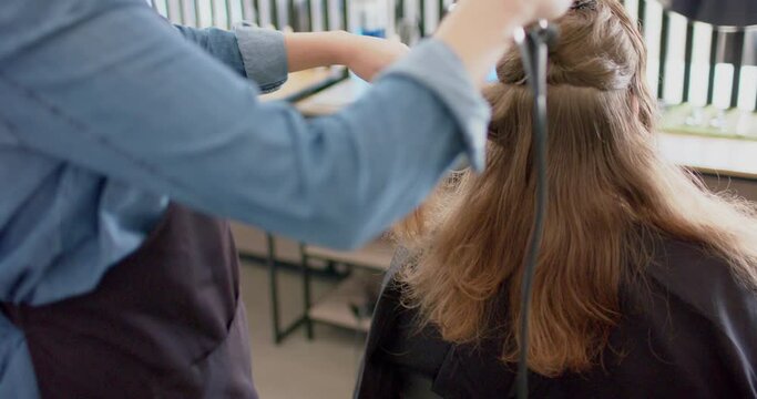 Caucasian female hairdresser styling client's long hair with brush and hairdryer, in slow motion