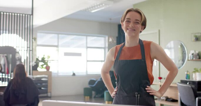 Portrait of caucasian female hairdresser in apron smiling at hair salon, copy space, slow motion