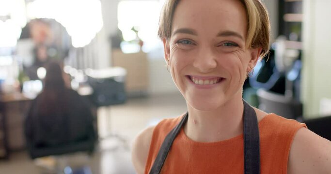 Portrait of happy caucasian female hairdresser in apron smiling at hair salon, slow motion