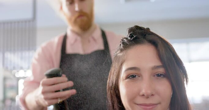 Caucasian male hairdresser spraying happy female client's hair with water at salon, slow motion