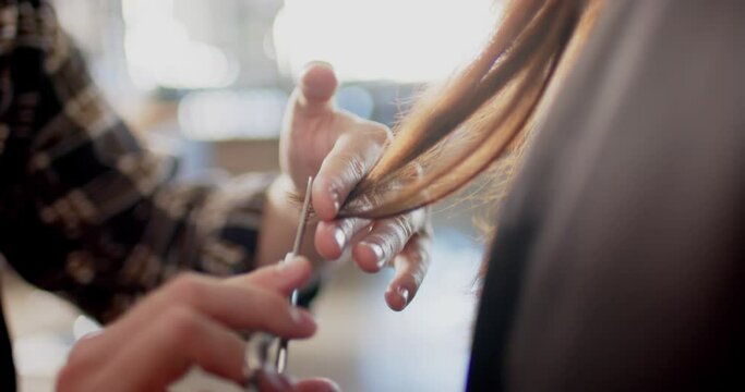 Hands of caucasian male hairdresser cutting ends of client's long hair with scissors, in slow motion