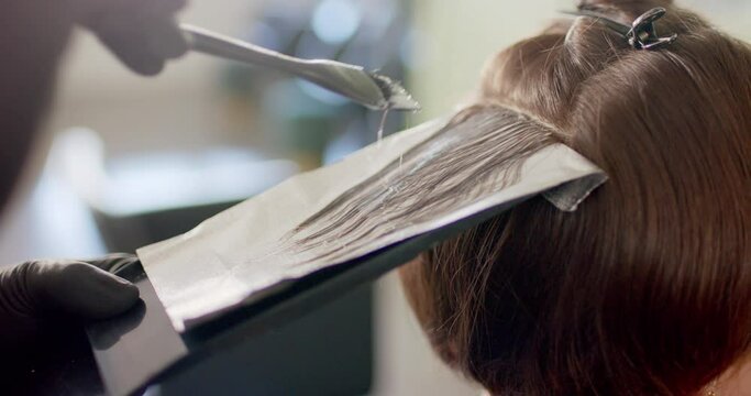 Close up of hairdresser highlighting client's hair with brush and foil at salon, in slow motion