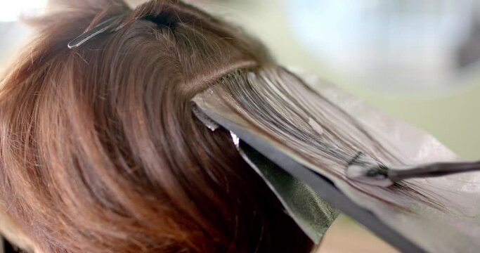 Close up of hairdresser highlighting client's hair with brush and foil at hair salon, in slow motion