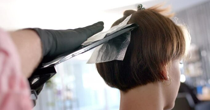 Hands of hairdresser using foil for highlighting client's hair at hair salon, in slow motion