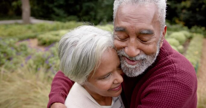 Happy senior biracial couple embracing and smiling in garden, unaltered, in slow motion