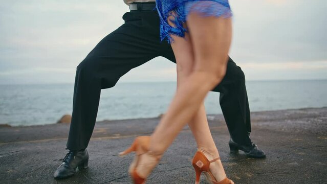 Closeup dancers legs performing sensual latin dance steps on overcast seashore.