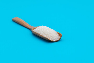 Wooden scoop with sugar crystals on blue background