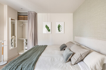 Comfortable bright bedroom with double bed and an empty wardrobe for clothes with beige wallpaper and cute pictures on the wall. The concept of moving to a new apartment
