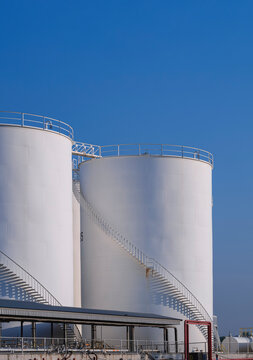 White storage fuel tanks with Oil pipeline system in industrial refinery yard area against blue sky background in vertical frame