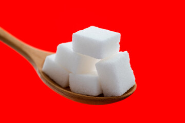 Sugar cubes in wooden spoon on red background