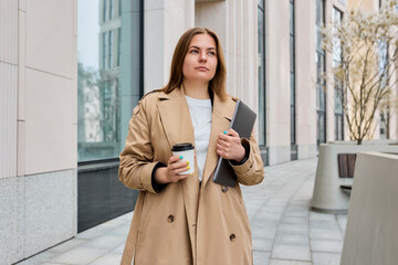 Business woman takes a break from her hectic day, outside in a chic trench coat, laptop in her hand