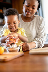 Cheerful African-American mother and son squeezing an orange to make orange juice. Son helps mother in the kitchen and have fun