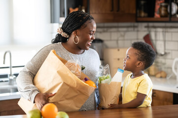 Cheerful African-American mother and son in the kitchen. Son helps a mother to bring in groceries after a grocery-shopping