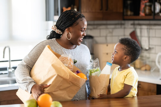 Cheerful African-American mother and son in the kitchen. Son helps a mother to bring in groceries after a grocery-shopping
