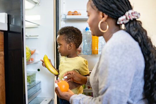 Cheerful African-American mother and son in the kitchen. Son helps a mother to bring in groceries after a grocery-shopping and put them into the refrigerator
