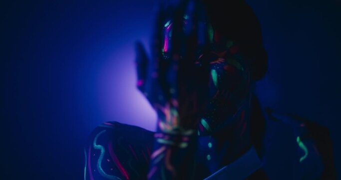 Young Dancer with Glowing Body Art Paint and White Clothes Creates Magic with Contemporary Dance Solo Routine. Choreographer Gestures Hands in a Modern Dance Show on a Dark Stage with a Single Light