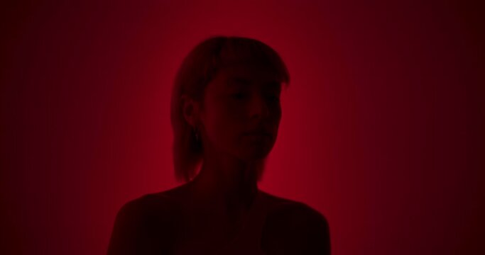 Beauty Close Up Portrait of a Young Caucasian Female with Blond Hair and Mullet Haircut Posing with Confidence in a Low Key Studio with Vivid Red Background. Model Footage with Artistic Appearance