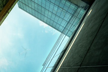 Fototapeta na wymiar Bottom up view of modern sustainable glass office building and airplane flying in blue sky. Exterior view of corporate headquarters glass building architecture. Energy-efficient building. Glass window