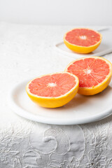 Fototapeta na wymiar Top view of cut red grapefruits on plate and white tablecloth, vertical, with copy space
