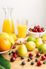 Close-up of bottle and glass with orange juice with oranges, lemons, cherries, pears and blueberries on table, white background, vertical, with copy space