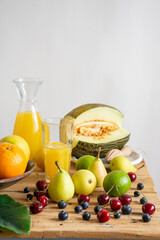Rustic table top view with melon, oranges, lemons, cherries, pears and bottle and glass with orange juice, white background, vertical, with copy space