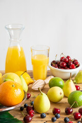Top view of bottle and glass with orange juice with oranges, lemons, cherries, pears and blueberries on table, white background, vertical, with copy space
