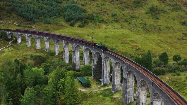 Drone shot circling the Jacobite train crossing the Glenfinnan bridge in Scotland