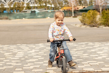 smiling little child girl riding a bike on the sidewalk at sunny day outdoors