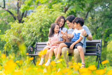 Happy Asian family parent and little kids enjoy and fun outdoor lifestyle on summer holiday vacation. Father, mother and child playing and resting together at park. Family relationship concept.