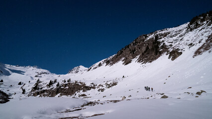 Skiers touring at night in the French alps in winter under the fullmoon light. fresh snow, stars, night sky