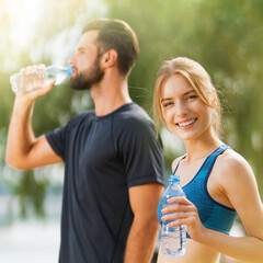 Portrait photo of happy smile, excited couple holding plastic water bottles, woman and man, bearded coach trainer, after successful morning training, sunrise outdoors. Fitness, sport, workout concept.