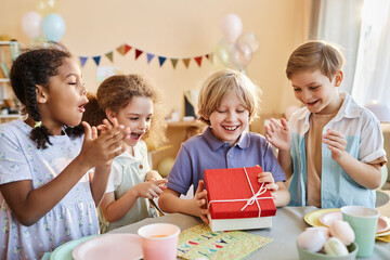 Diverse group of happy children at Birthday party with excited boy opening presents