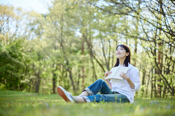 Naklejka na ściany i meble 森の中でリラックスしながら読書をする30代日本人女性の初夏のイメージ