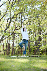 自然豊かな初夏の森でくつろぎながらヨガを楽しむ日本人女性