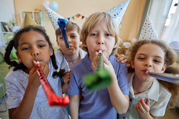 Front view portrait of three children holding party blowers and having fun at Birthday celebration