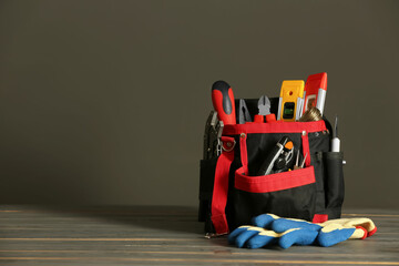 Bag with different tools for repair and protective gloves on wooden table, space for text