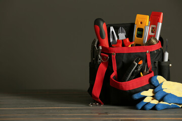 Bag with different tools for repair and protective gloves on wooden table, space for text