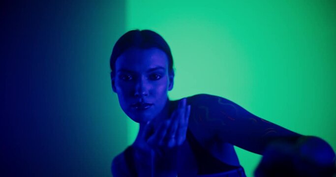 Young Dancer Delivers Captivating Improvised Contemporary Dance Performance, Adorned in Vibrant Body Paint and Stylish Clothes, Against a Colorful Background in a Dark Space. Slow Motion Footage