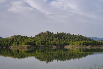 Scenic view of a calm lake with the reflections of the forested hill and the sky